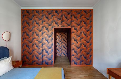 A room with a distinctive fern-patterned orange wallpaper and an open doorway.