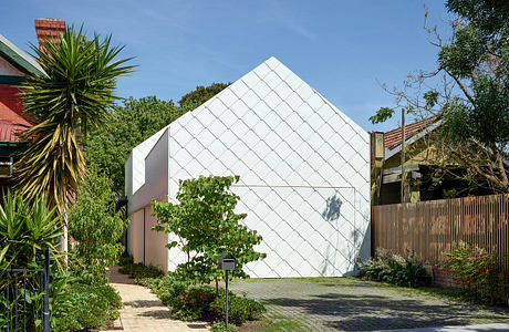 Geometric white house with a diamond-pattern facade surrounded by greenery.