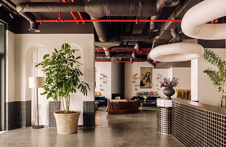 Modern office interior with exposed red pipes, ductwork, and stylish furniture.