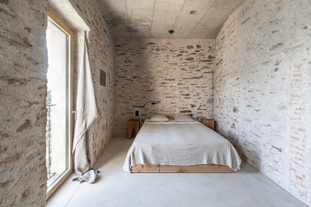 Minimalist bedroom with exposed stone walls and concrete floor.