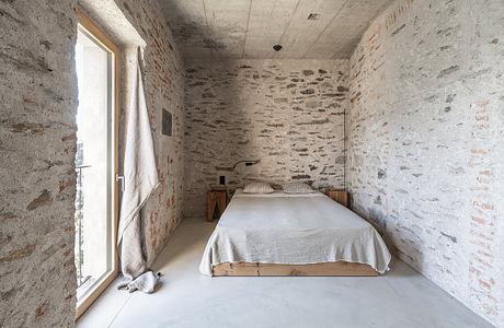 Minimalist bedroom with exposed stone walls and concrete floor.