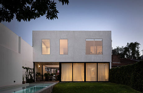 Modern two-story house with illuminated windows and a pool at dusk.