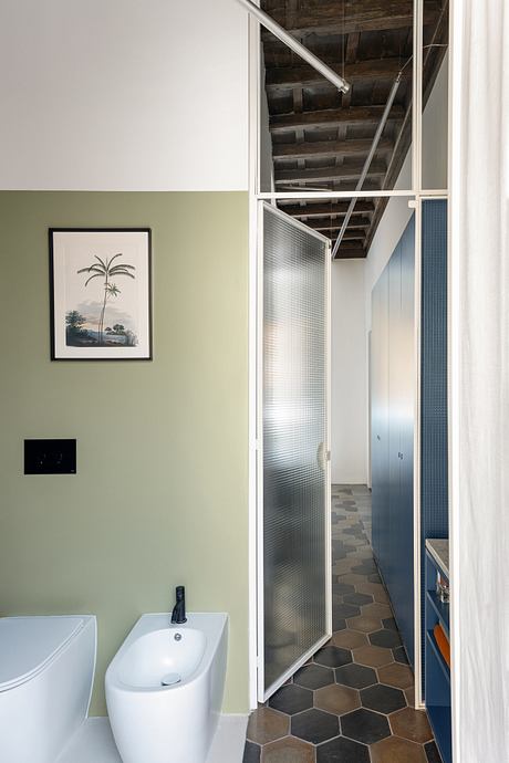 Modern bathroom with green walls, frosted glass door, and exposed ceiling beams.