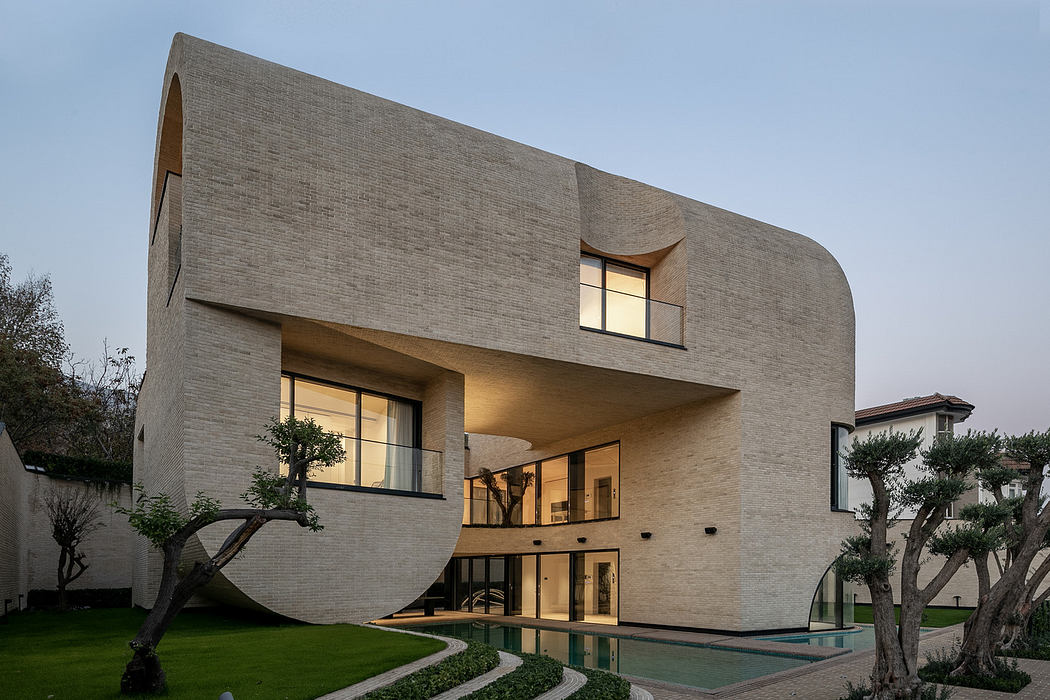 Modern house with curved design, large windows, and a pool at twilight.