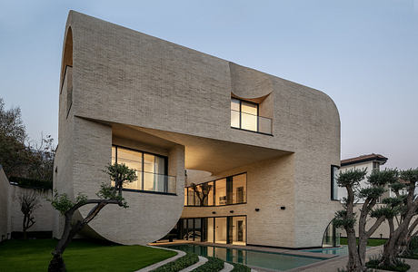 Modern house with curved design, large windows, and a pool at twilight.