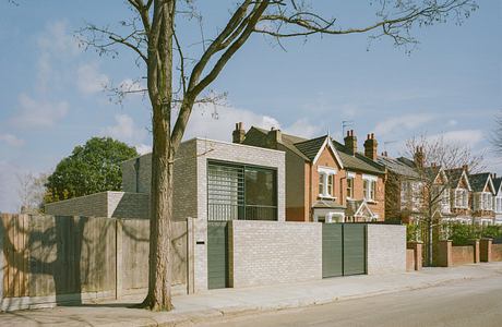 Modern house with brick facade and large windows next to traditional homes.