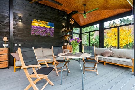 Modern living room with wooden accents, furniture, and large windows showing fall foliage.