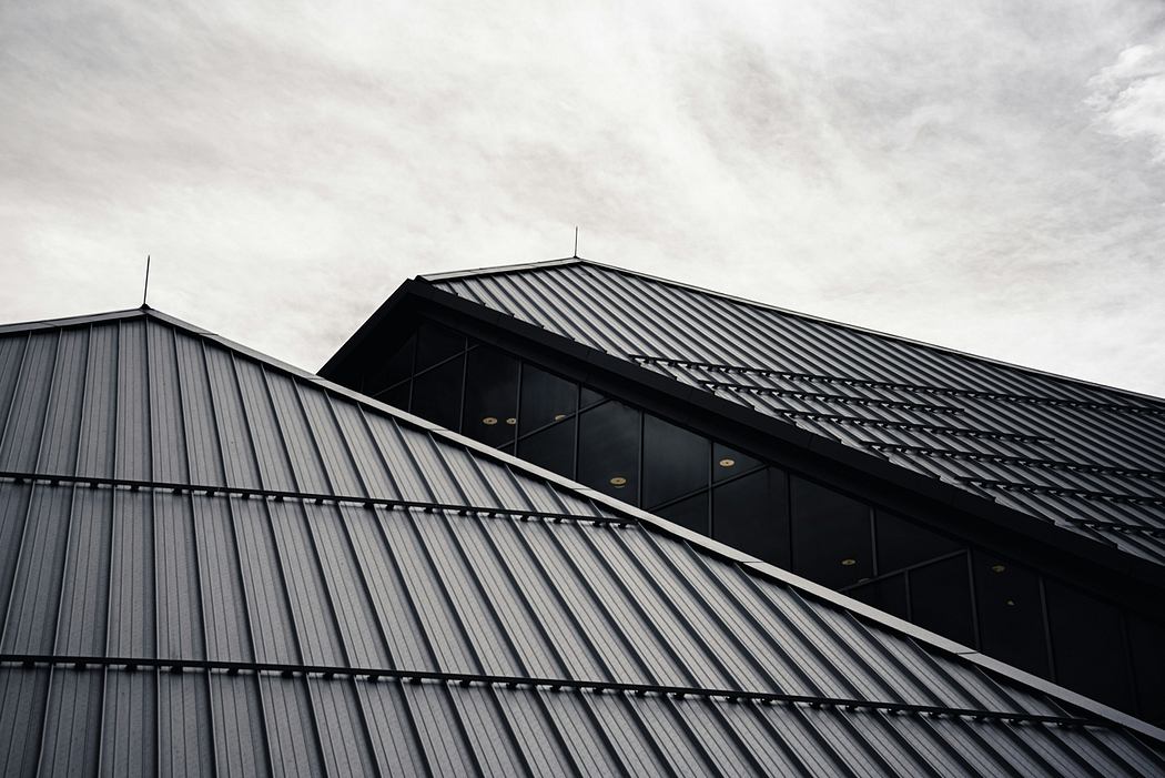 A geometric building facade with metal cladding and glass windows against a cloudy sky.