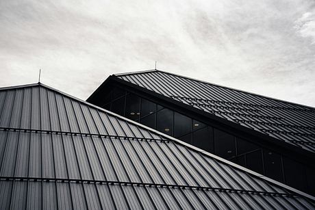 A geometric building facade with metal cladding and glass windows against a cloudy sky.