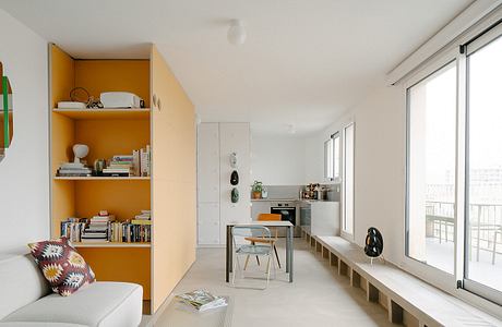 Bright apartment interior with orange shelving unit and floor-to-ceiling windows.