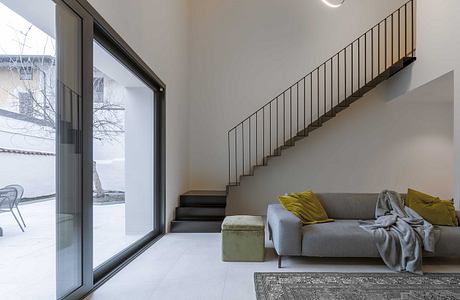 Modern living room with a sofa, staircase, and large window.