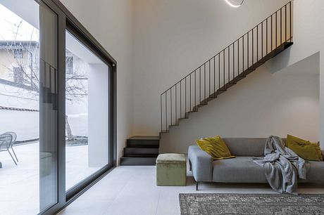 Modern living room with a sofa, staircase, and large window.