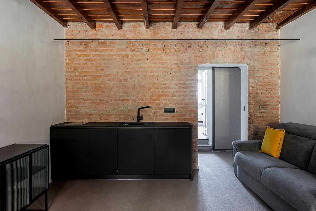 Modern kitchen with sleek black cabinetry, exposed brick wall, and wooden ceiling beams.