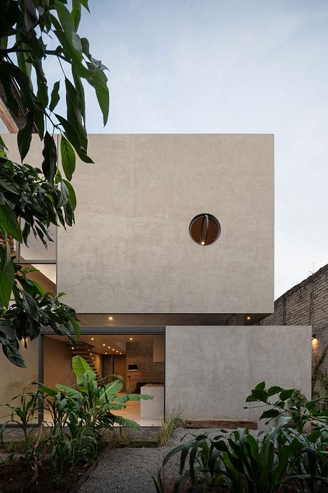 Modern minimalist building with circular window and garden.