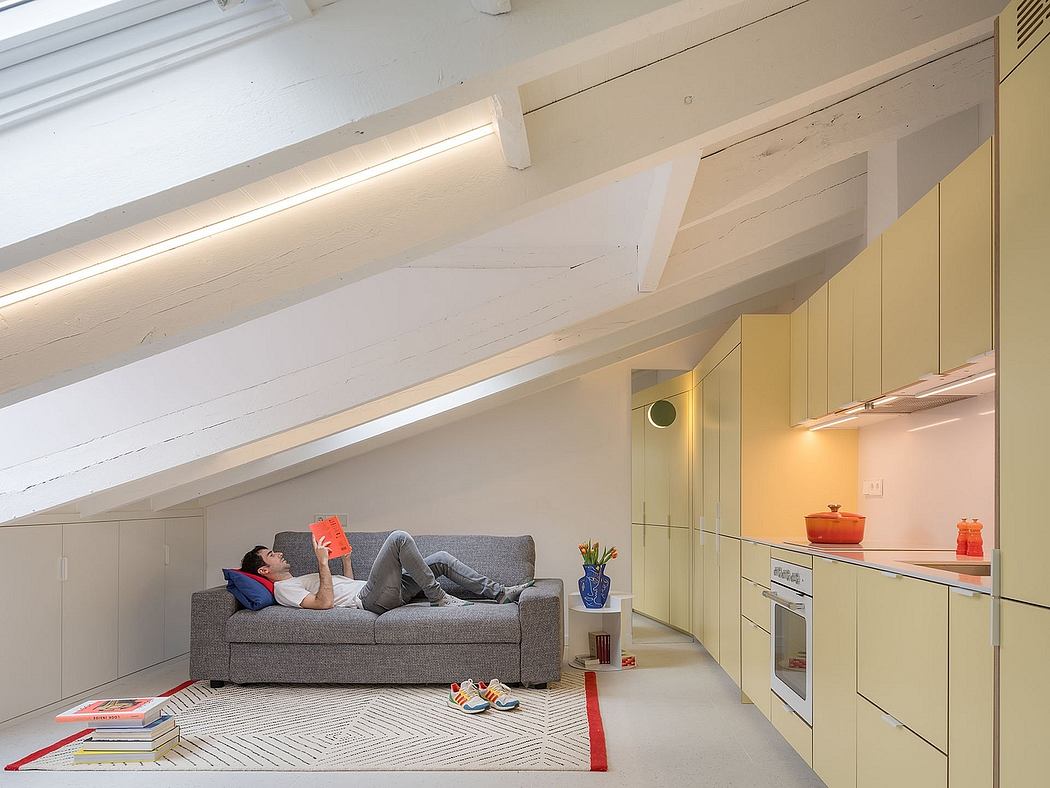 Cozy attic living space with modern furniture, warm lighting, and minimalist kitchen.
