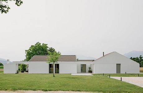 Modern single-story building with tiled roof, large windows, and lush surrounding landscape.