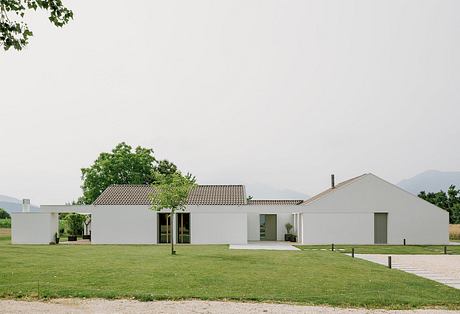 Modern single-story building with tiled roof, large windows, and lush surrounding landscape.