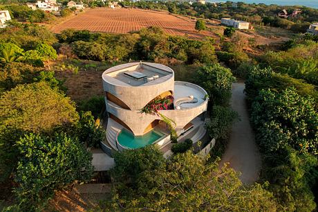 Striking architectural design with circular structures, terraces, and a pool nestled in lush greenery.