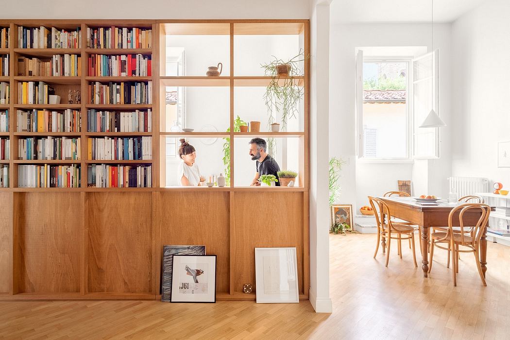 Bright Scandinavian-style dining room with wooden bookshelf partition and two people chatting.