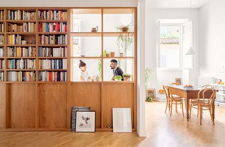 Bright Scandinavian-style dining room with wooden bookshelf partition and two people chatting.