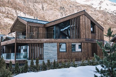 A rustic wooden lodge with a curved roof and large windows overlooking a snowy landscape.