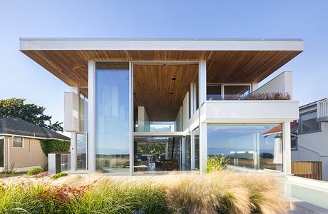 Modern glass house with a wooden overhang and landscaped garden.