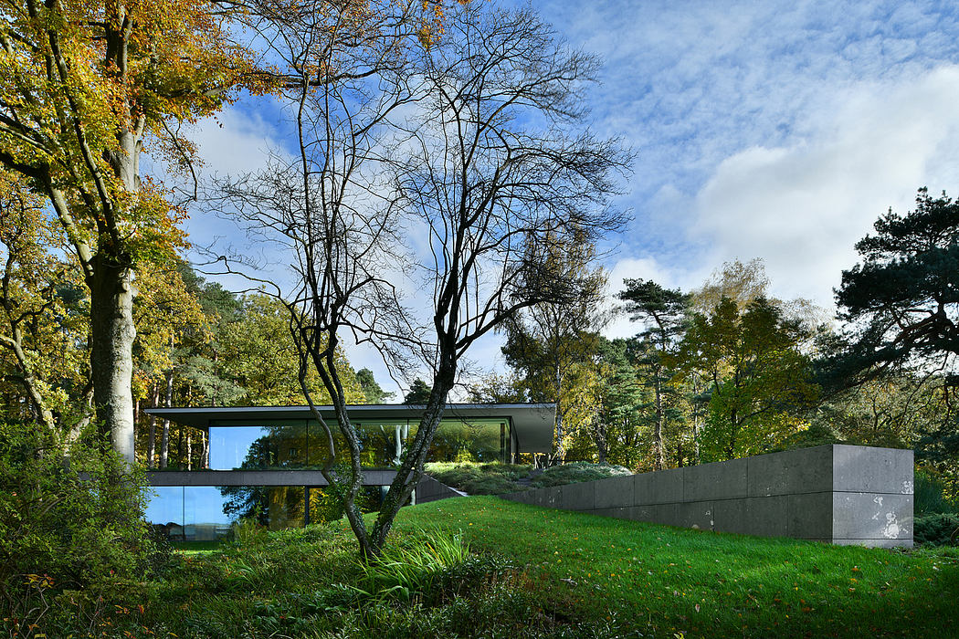 Modern glass house with concrete walls surrounded by autumn trees.