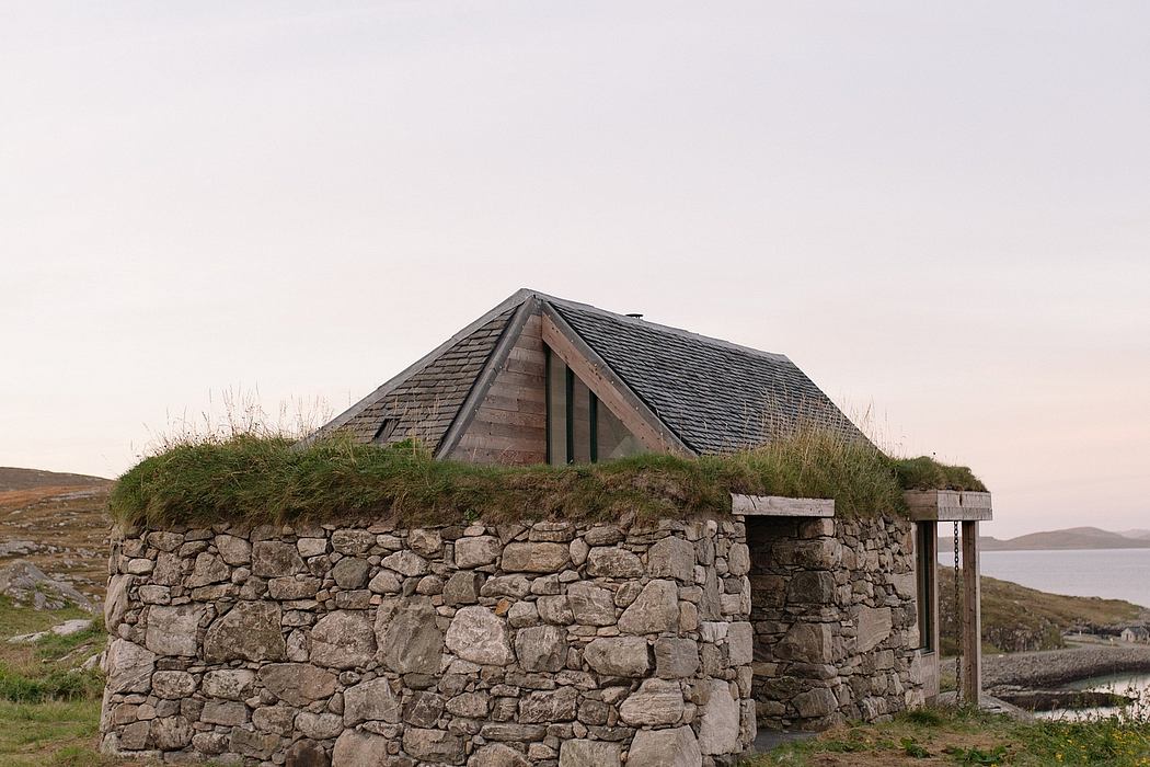 Rustic stone structure with a wooden roof set against a tranquil landscape.