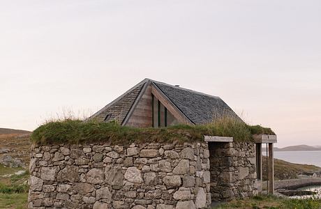 Rustic stone structure with a wooden roof set against a tranquil landscape.