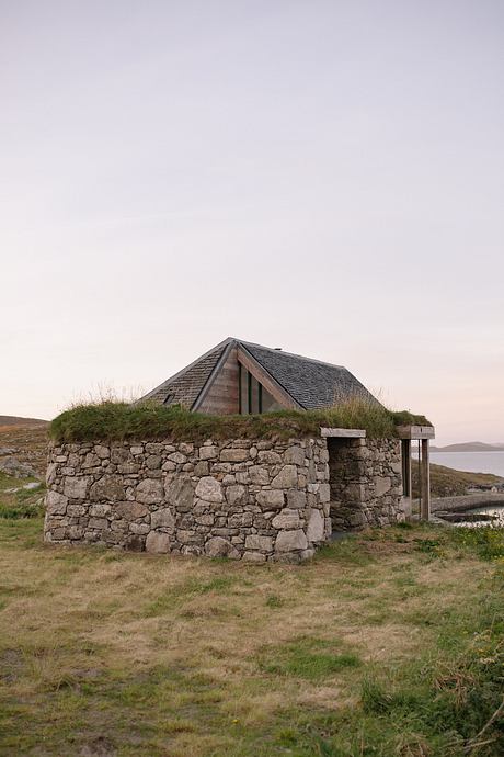 Rustic stone structure with a wooden roof set against a tranquil landscape.