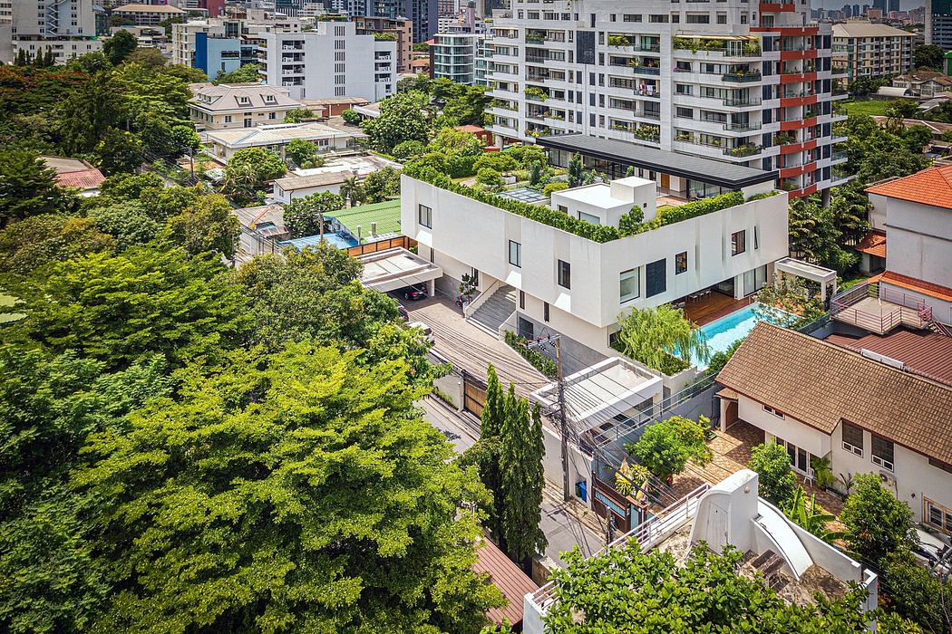 Modern white building with rooftop garden surrounded by trees in an urban area.
