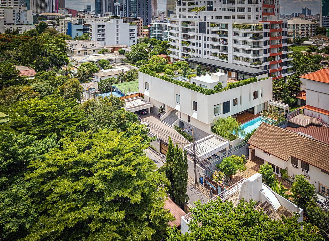 Modern white building with rooftop garden surrounded by trees in an urban area.