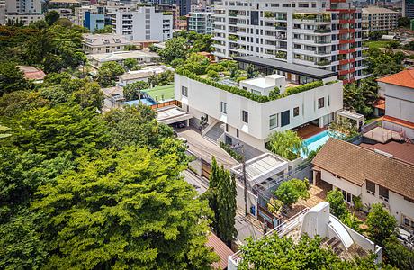 Modern white building with rooftop garden surrounded by trees in an urban area.