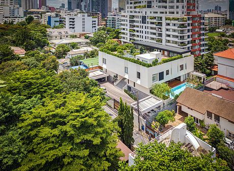 Modern white building with rooftop garden surrounded by trees in an urban area.