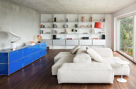 A modern living room with a white sofa, blue storage unit, and floor-to-ceiling bookshelves.