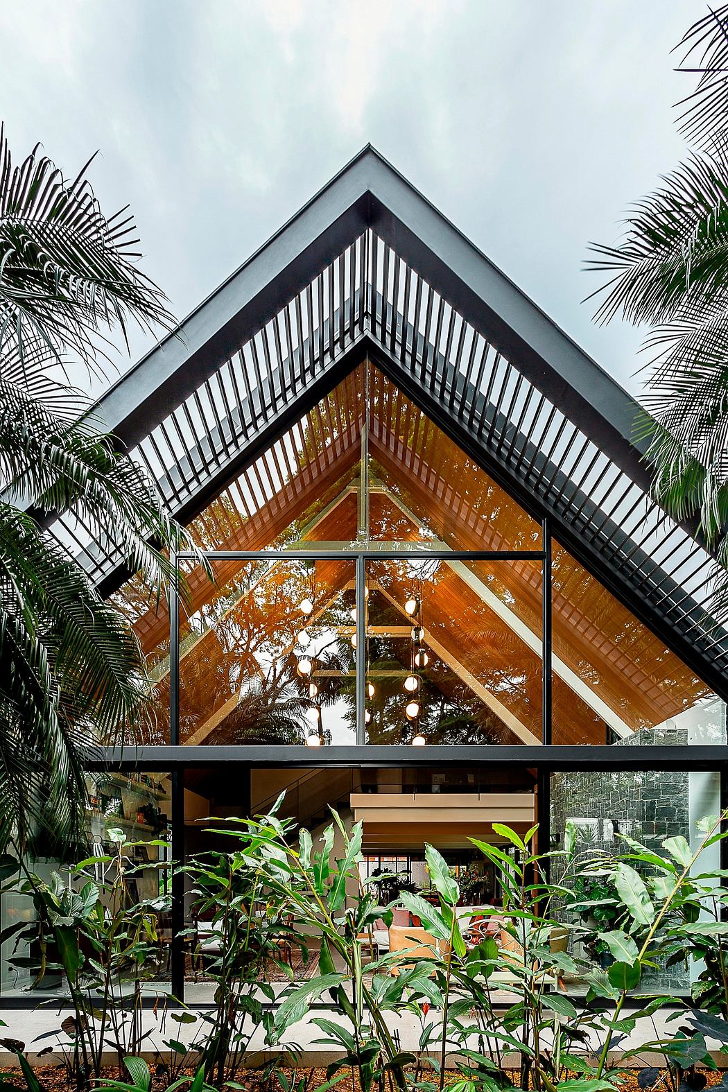 Modern A-frame house with large glass windows surrounded by greenery.