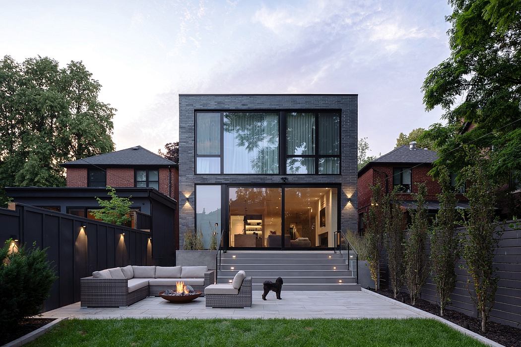 Modern two-story home with large windows, outdoor seating, and a dog.