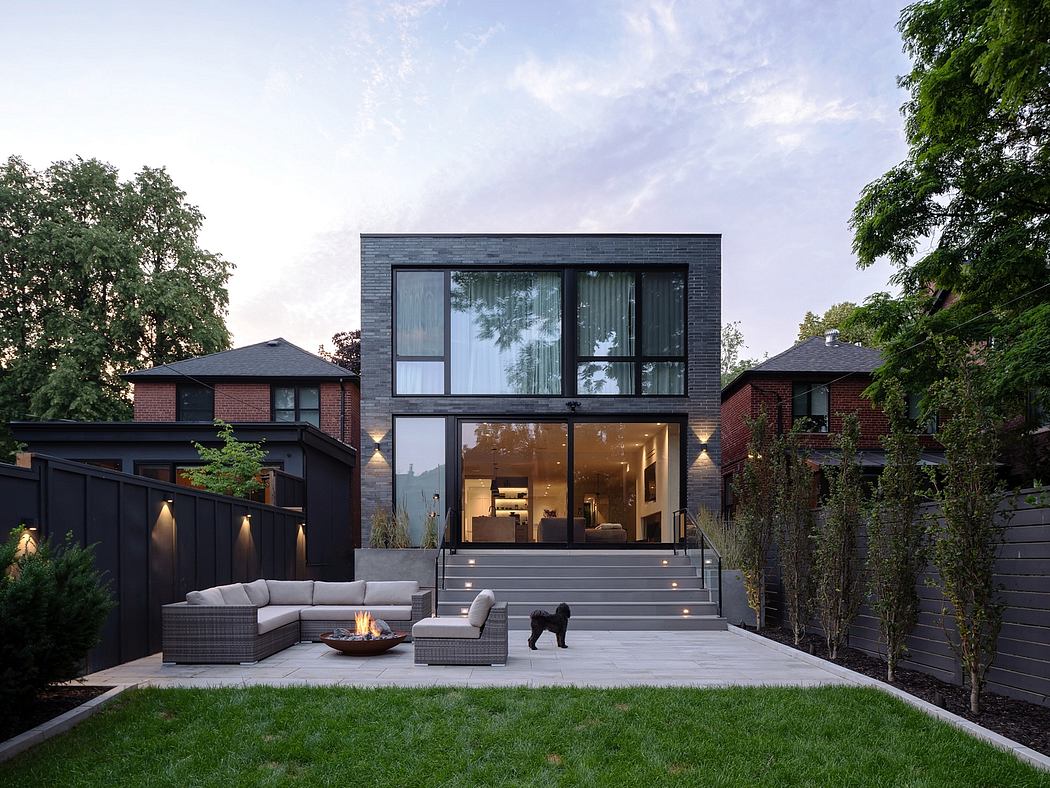 Modern two-story home with large windows, outdoor seating, and a dog.