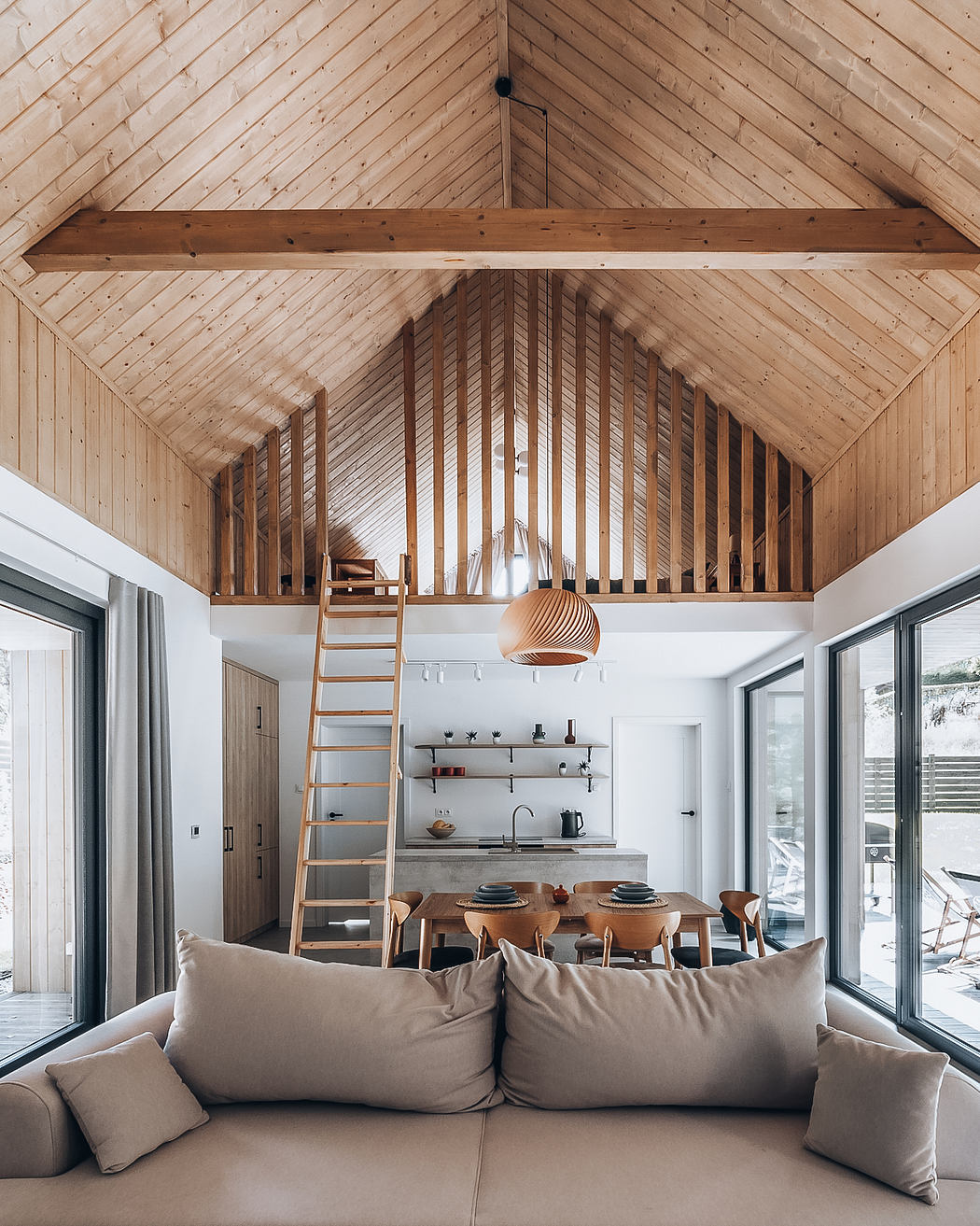 A cozy, modern cabin interior with a vaulted wooden ceiling, ladder, and open-concept living space.