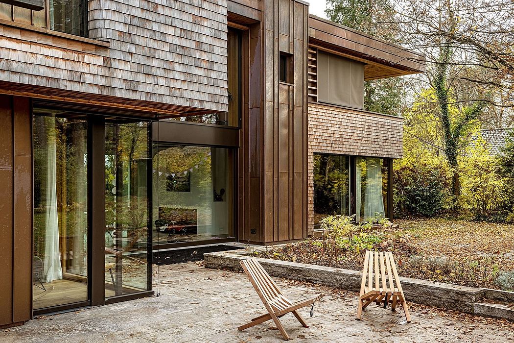 Contemporary house with wooden slats and large windows overlooking a garden with two chairs