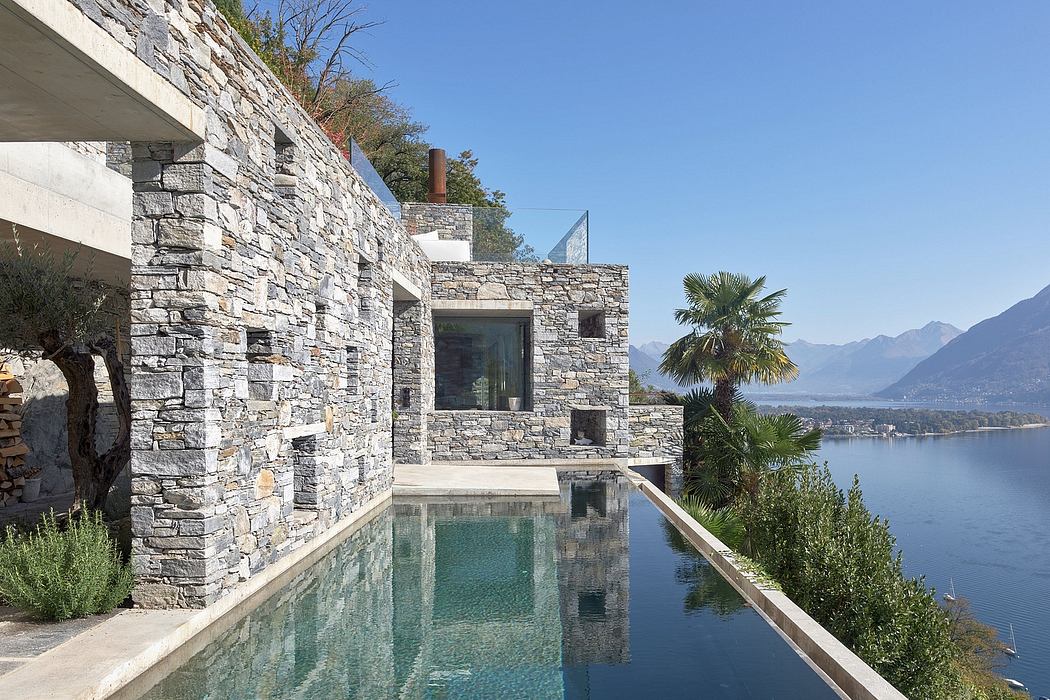 Stone-clad house with infinity pool overlooking a lake.