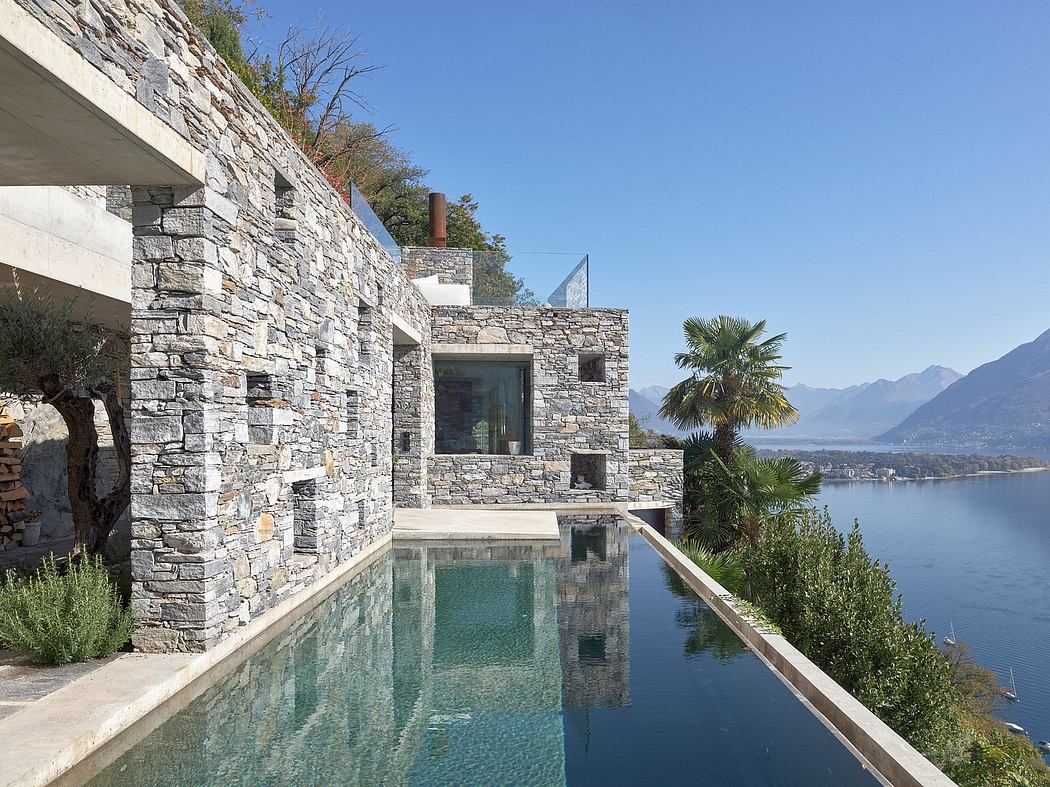 Stone-clad house with infinity pool overlooking a lake.