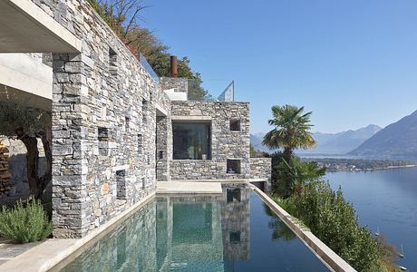 Stone-clad house with infinity pool overlooking a lake.