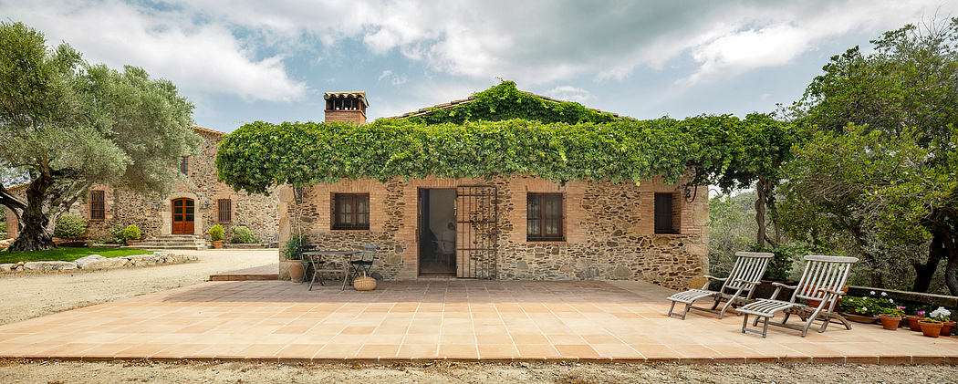 An inviting rustic stone farmhouse with ivy-covered exterior and terrace seating.