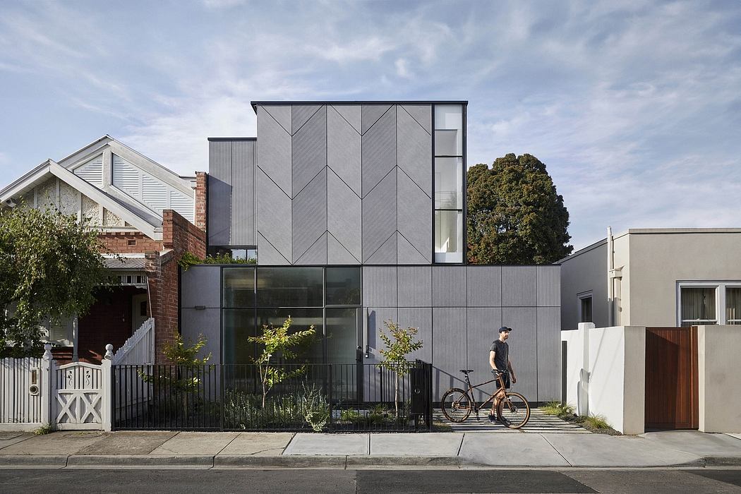 A modern gray building with geometric patterns and large glass windows, a person and a bicycle visible.
