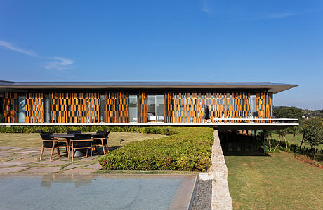 Modern single-story building with a striking orange and brown facade, surrounded by lush greenery.