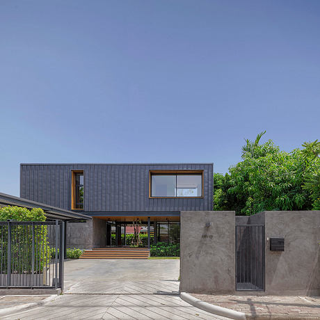 Modern 2-story house with gray siding, large windows, and a concrete entryway surrounded by lush greenery.