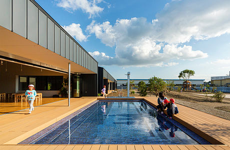 Modern exterior of a building with a pool, deck, and surrounding landscaping. The architecture features a mix of glass, metal, and natural materials.