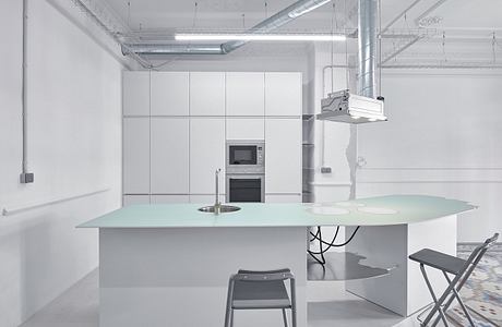 A modern, minimalist kitchen with sleek white cabinetry, ample counter space, and a large central table.