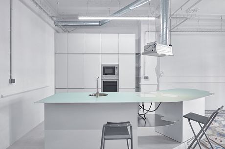 A modern, minimalist kitchen with sleek white cabinetry, ample counter space, and a large central table.